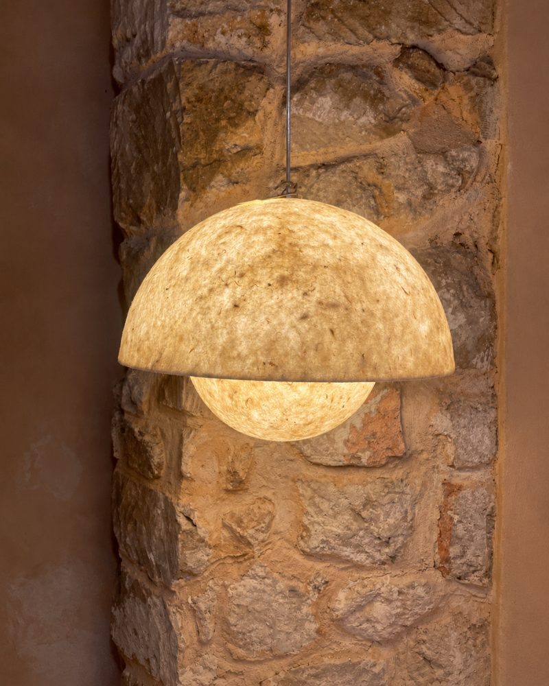 Natural felt pendant lamp glowing against a stone wall